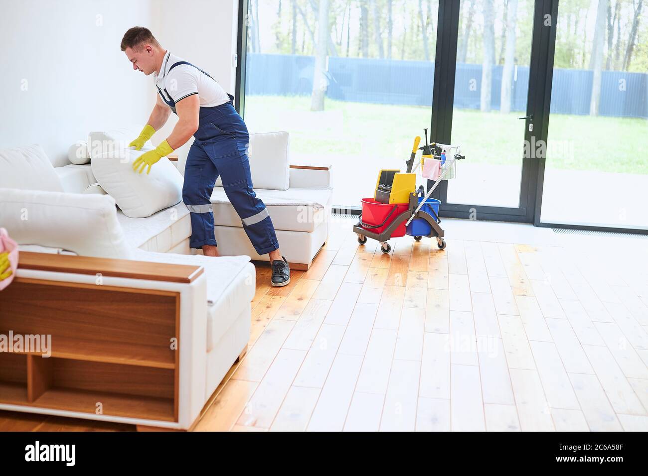 man dressed in blue uniform clean leather sofa, cleaning trolley with