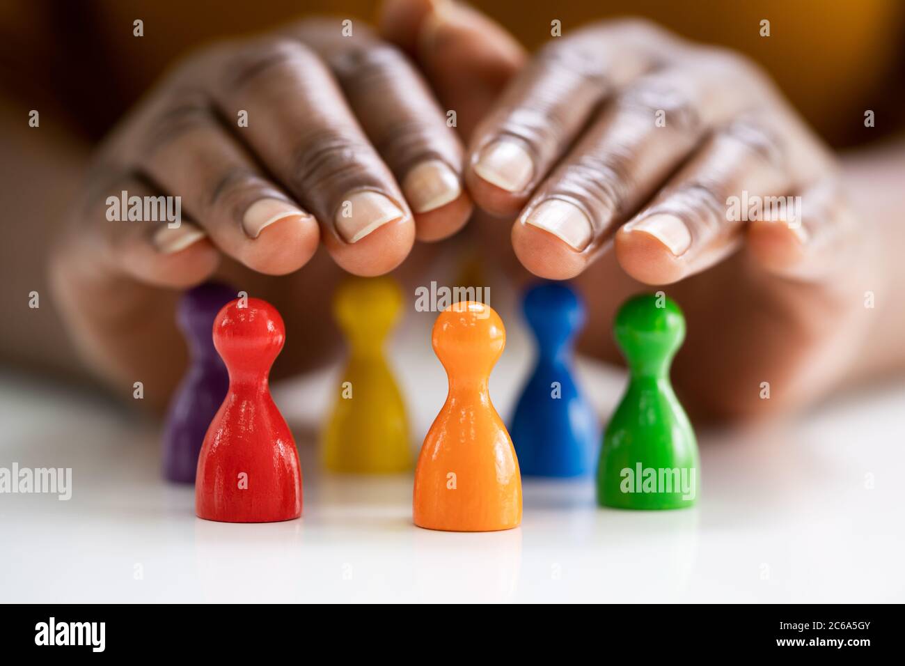 Diversity And Inclusion Concept. Hand Protecting Hand Colored Staff Pawns In Circle Stock Photo