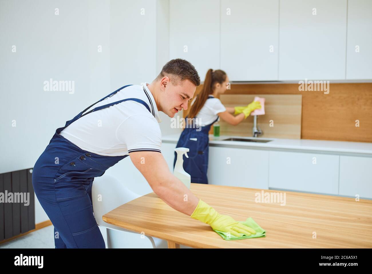 Cleaning staff. man in special equipment wiping dust off from table, background woman washing Stock Photo