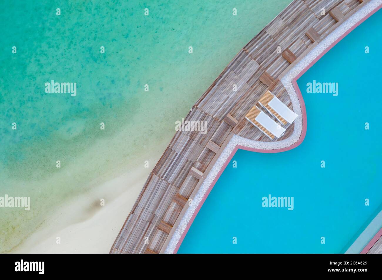 View from drone infinity swimming pool, loungers. Turquoise pool water over sandy beach and ocean lagoon Stock Photo