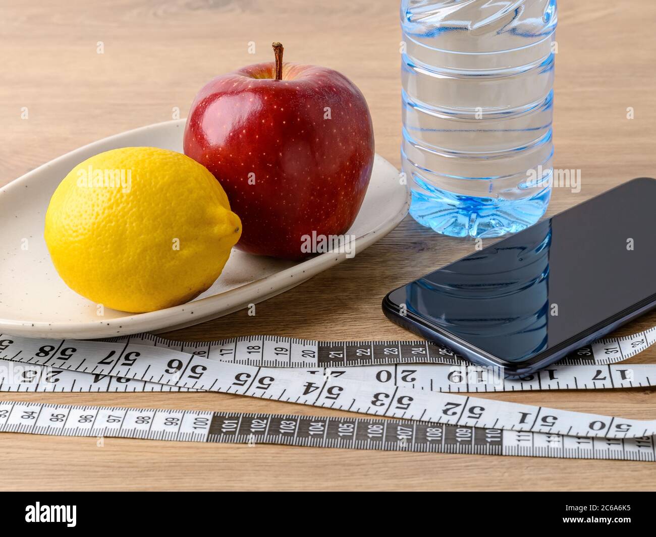 Measuring tape with centimeters and inches, smartphone, drinking water and fruits on a brown table. Healthy eating, diet, weight loss and body slim. Stock Photo