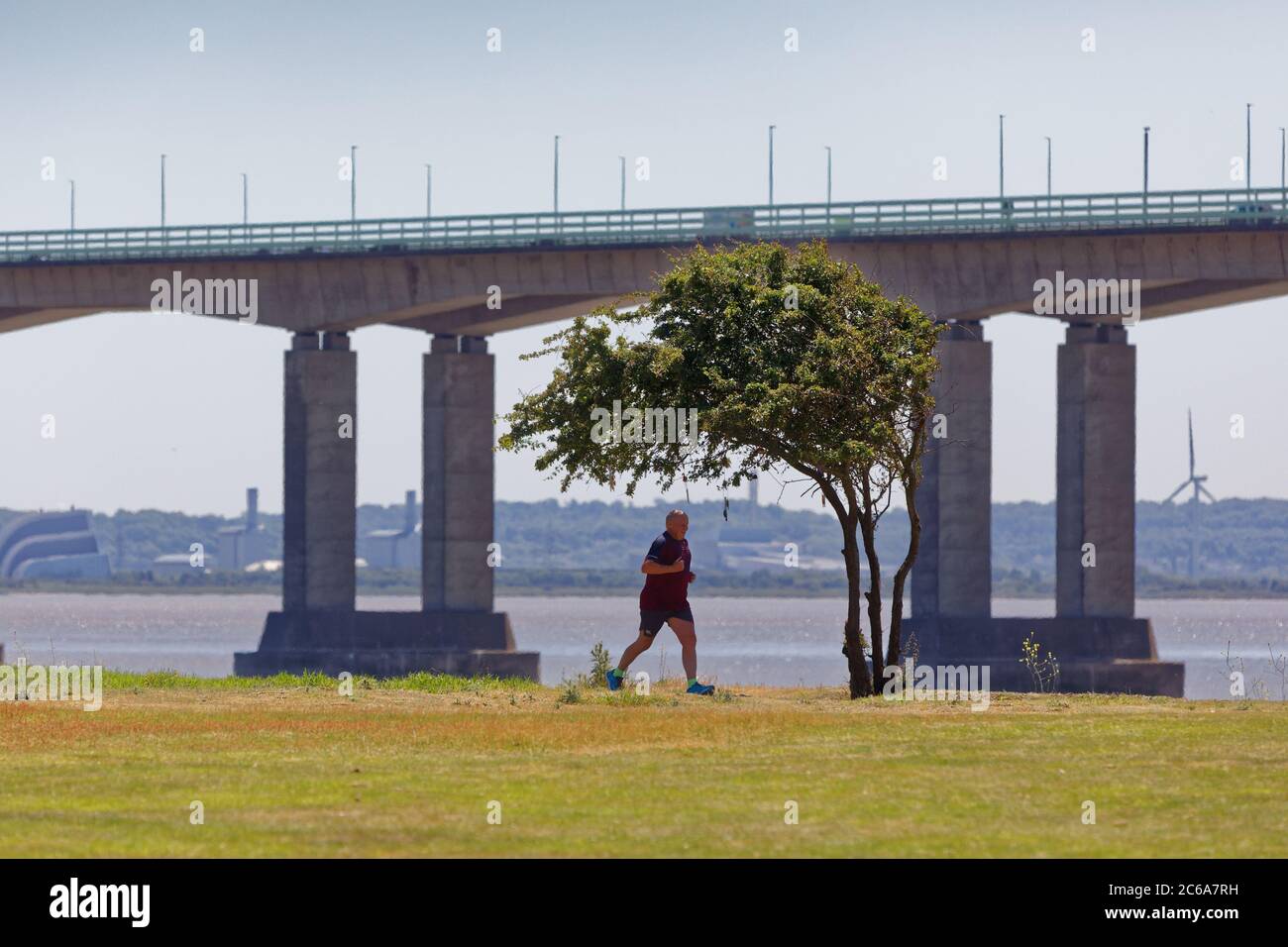 A man runs along the path which runs alongside the river Severn estuary which overlooks the Prince of Wales Bridge as seen from Sudbrook in Monmouthsh Stock Photo