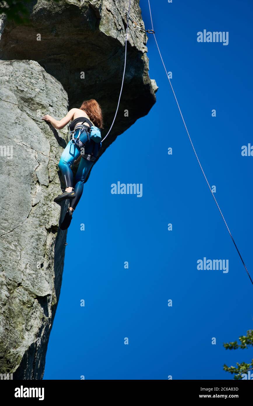 Vertical snapshot of female rock-climber, climbing up a cliff, wearing blue  leggings and a black