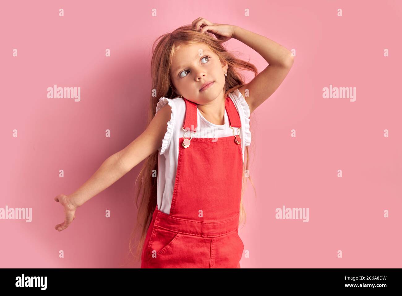 Portrait of dreamy caucasian kid girl wearing red overalls with long ...