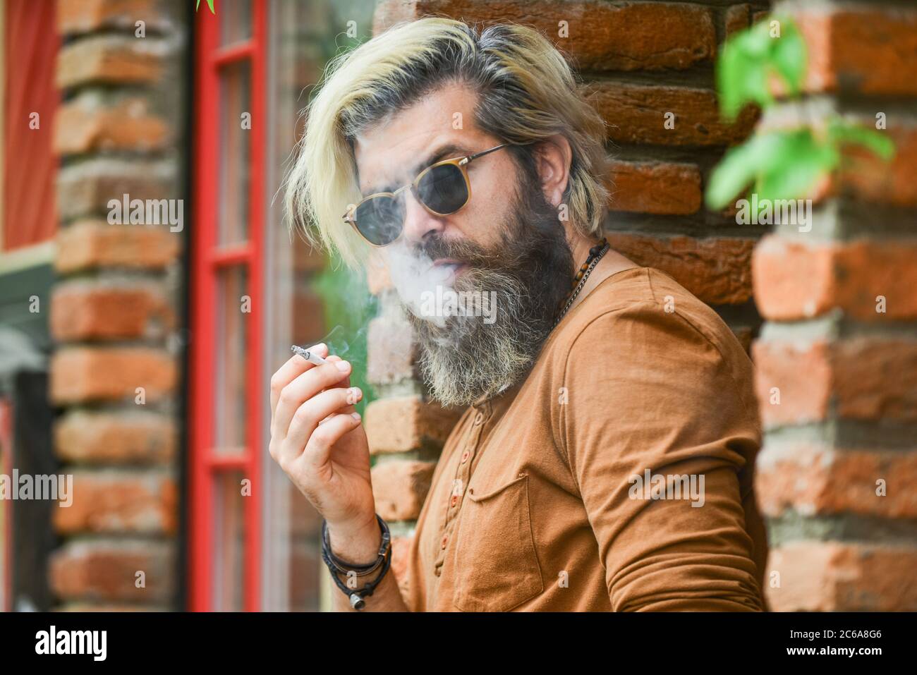 Smoking outdoors. Went on smoke break. Hipster smoking old architecture  background. Smoking habit. Fashionable mature man with cigarette. Brutal  guy sunglasses smoking tobacco. Cool guy relaxing Stock Photo