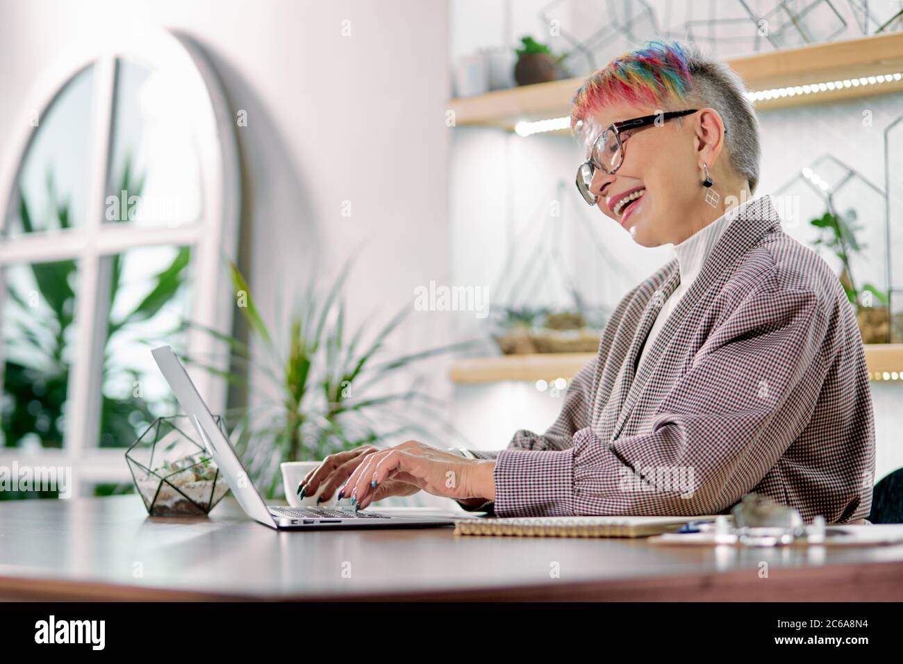 Using modern technologies by mature people. Gorgeous business woman with  short colorful hair wearing glasses and blazer sit looking at screen of  lapto Stock Photo - Alamy