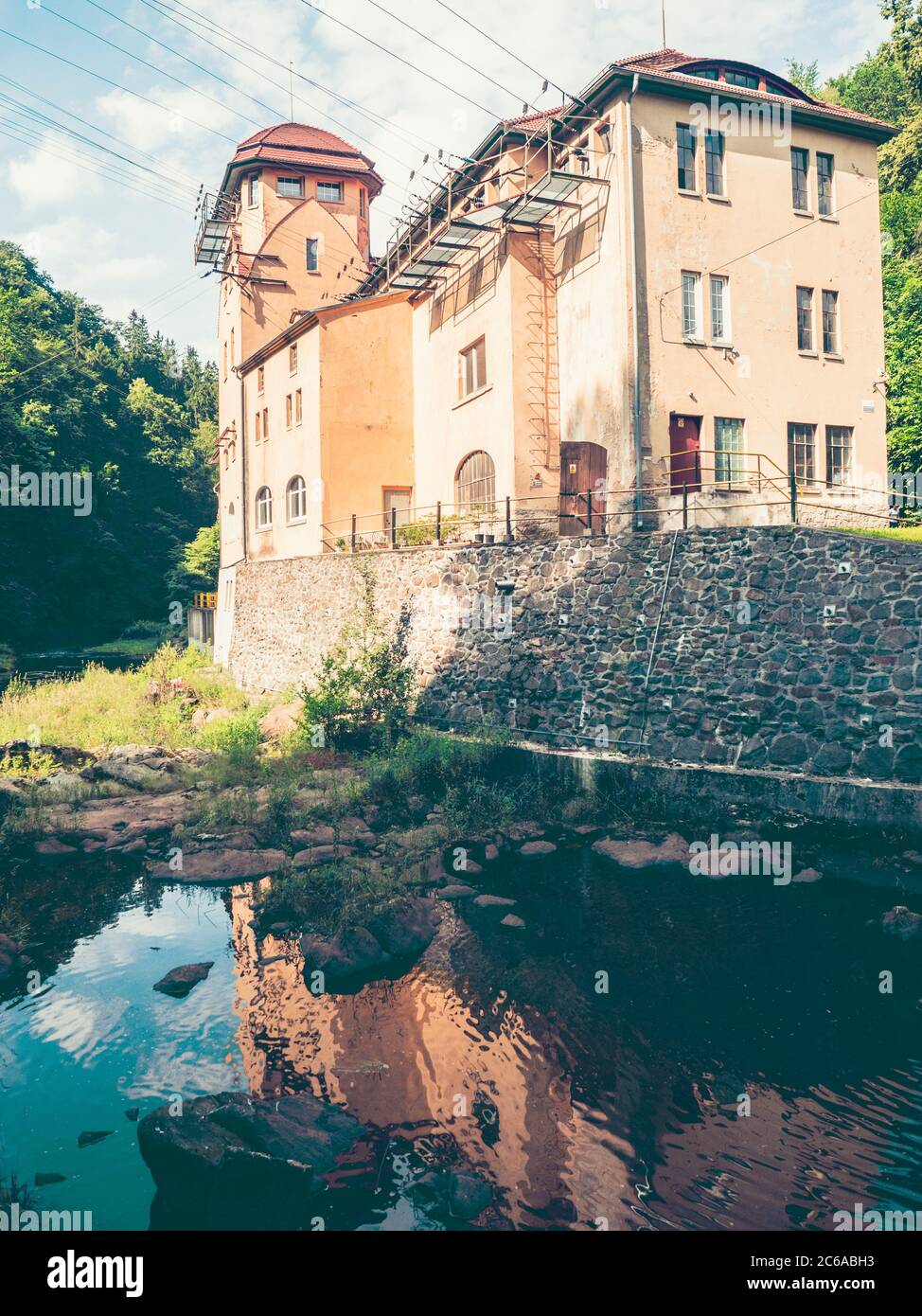 Old hydro power plant with empty riverbed, river Kwisa, Poland. The rest of water in water tank mirroring blue sky Stock Photo