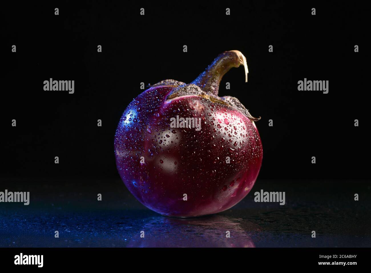 One wet round eggplant with a reflection on a black background. Isolated Stock Photo