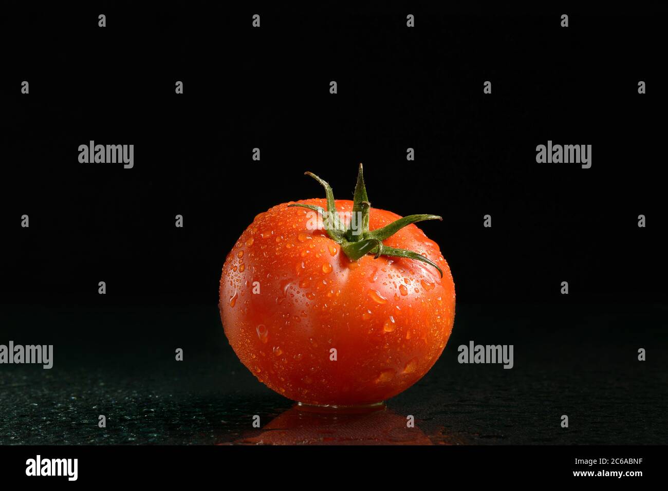 One ripe red tomato on a black background with water drops with reflection Stock Photo