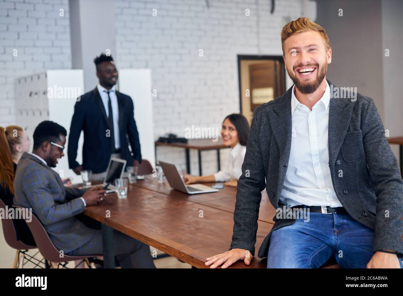 Positive man confidently looking at camera while his business partners have discussion in office Stock Photo