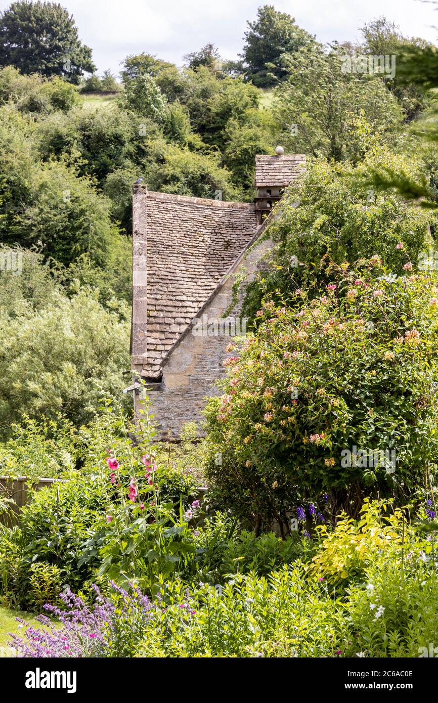 A glimpse of the old stone dovecote (c.1600 AD) seen across a summer garden in the Cotswold village of Naunton, Gloucestershire UK Stock Photo