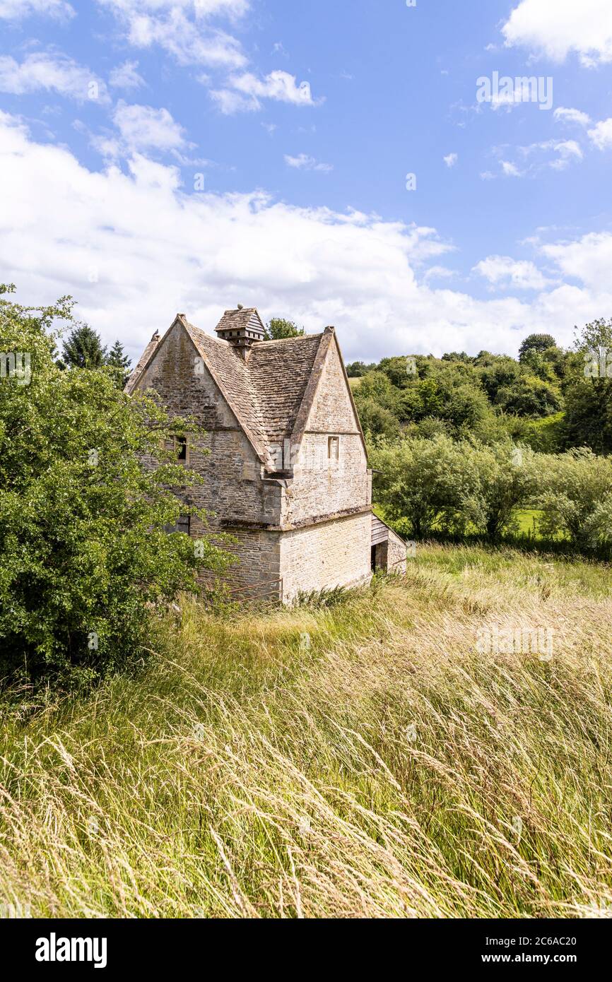 An old stone dovecote (c.1600 AD) beside the infant River Windrush as it flows through the Cotswold village of Naunton, Gloucestershire UK Stock Photo