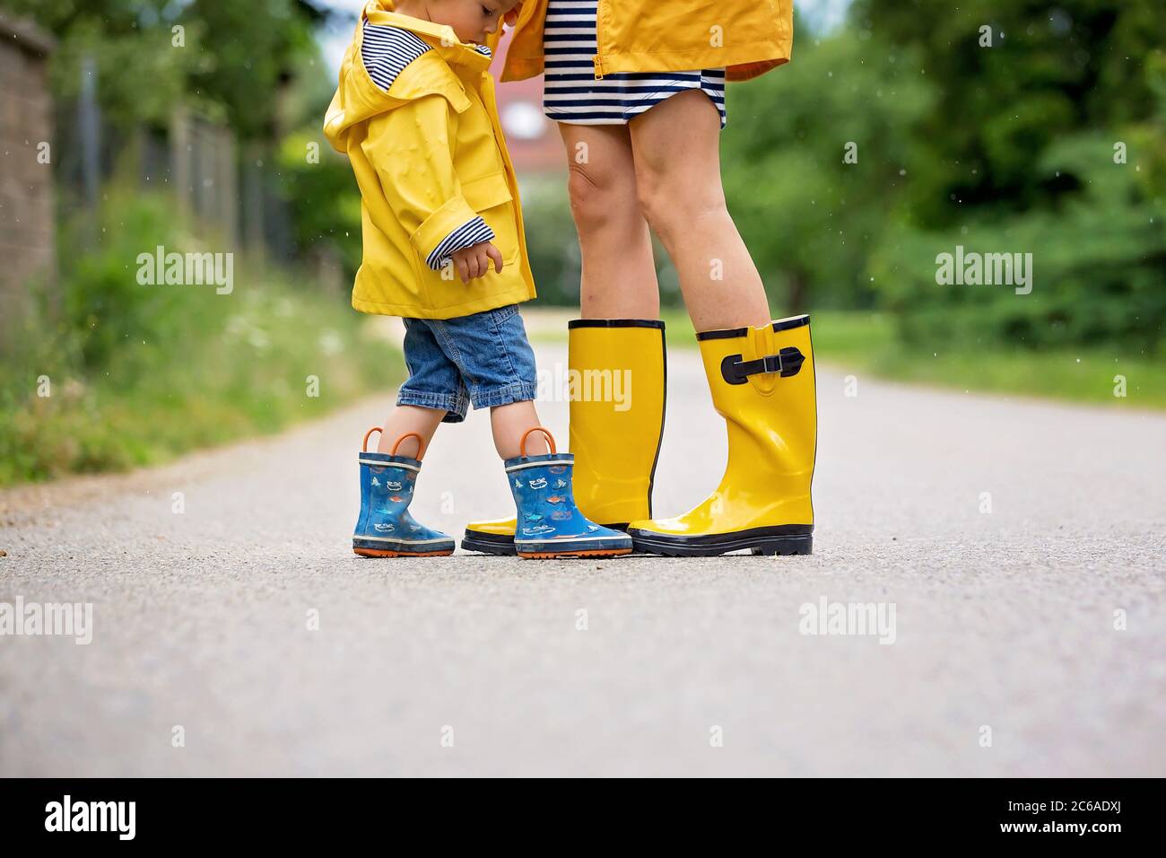 Mother and toddler child, boy, playing in the rain, wearing boots and