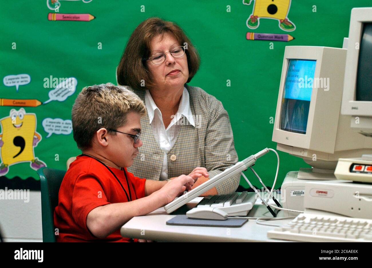 Mabank, Texas September 10, 2003: 12-year-old boy with Hurler's Syndrome with a full-time teacher's aide uses Intellikeys augmentative keyboard to type more easily on a computer in his 7th grade classroom. MODEL RELEASE SP-73 (boy student in red) SP-69 (aide)  ©Bob Daemmrich Stock Photo