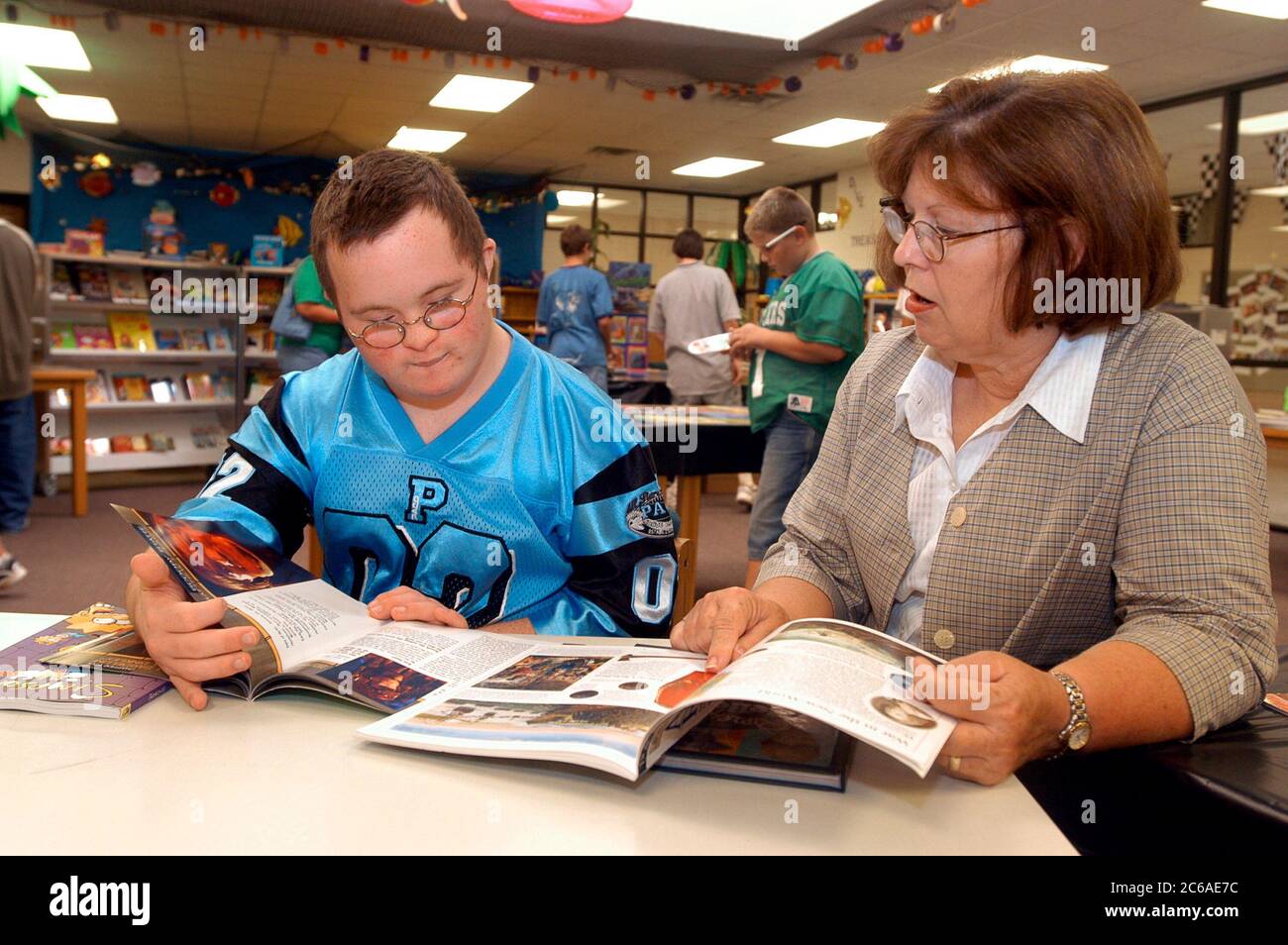 Mabank, Texas: September 10, 2003: Thirteen-year-old boy with Down syndrome in his middle school library, looking at books and interacting with a speech and hearing specialist.  MR SP75 (boy in blue) SP69  (adult)  ©Bob Daemmrich Stock Photo