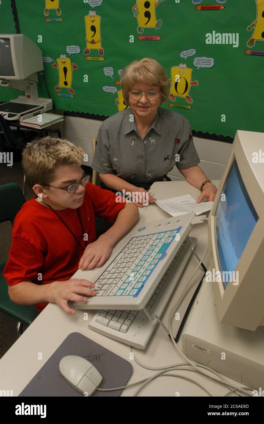 Mabank, Texas September 10, 2003: 12-year-old boy with Hurler's Syndrome with a full-time teacher's aide uses Intellikeys augmentative keyboard to type more easily on a computer in his 7th grade classroom. MODEL RELEASE SP-73 (boy student in red) SP-74 (aide)  ©Bob Daemmrich Stock Photo