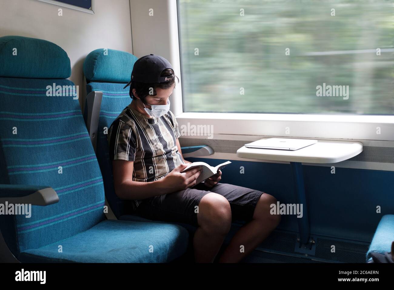 Boy reads book on commuters  train wearing face mask during  Covid-19 pandemic lockdown, London, UK Stock Photo