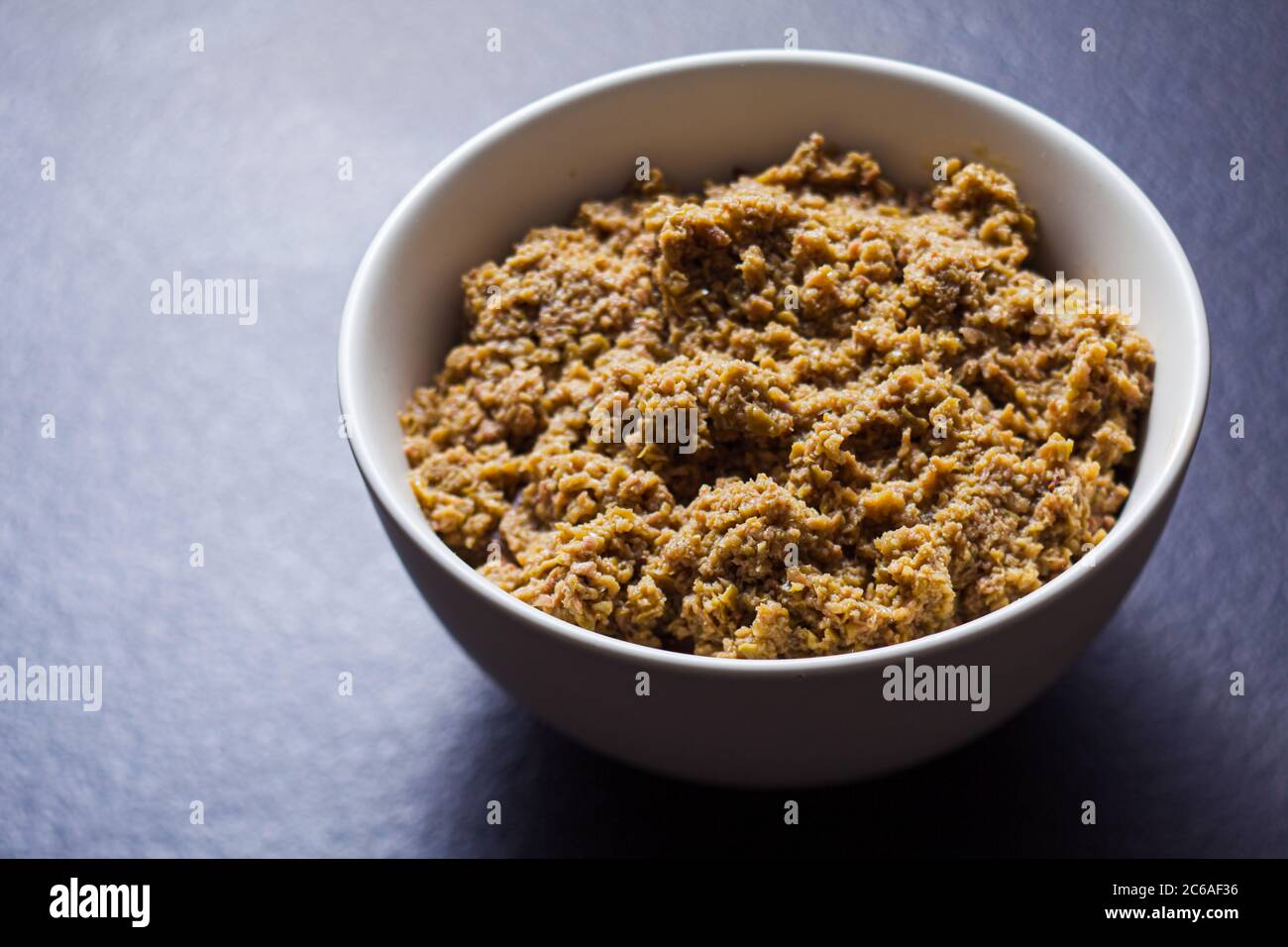 Ground olive spread in bowl on dark grey surface Stock Photo