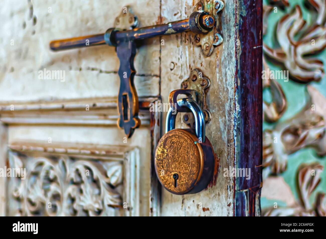 A brass padlock is suspended from a staple on a partially open door. An old fashioned and weather brass hasp is also visible in the image. Stock Photo