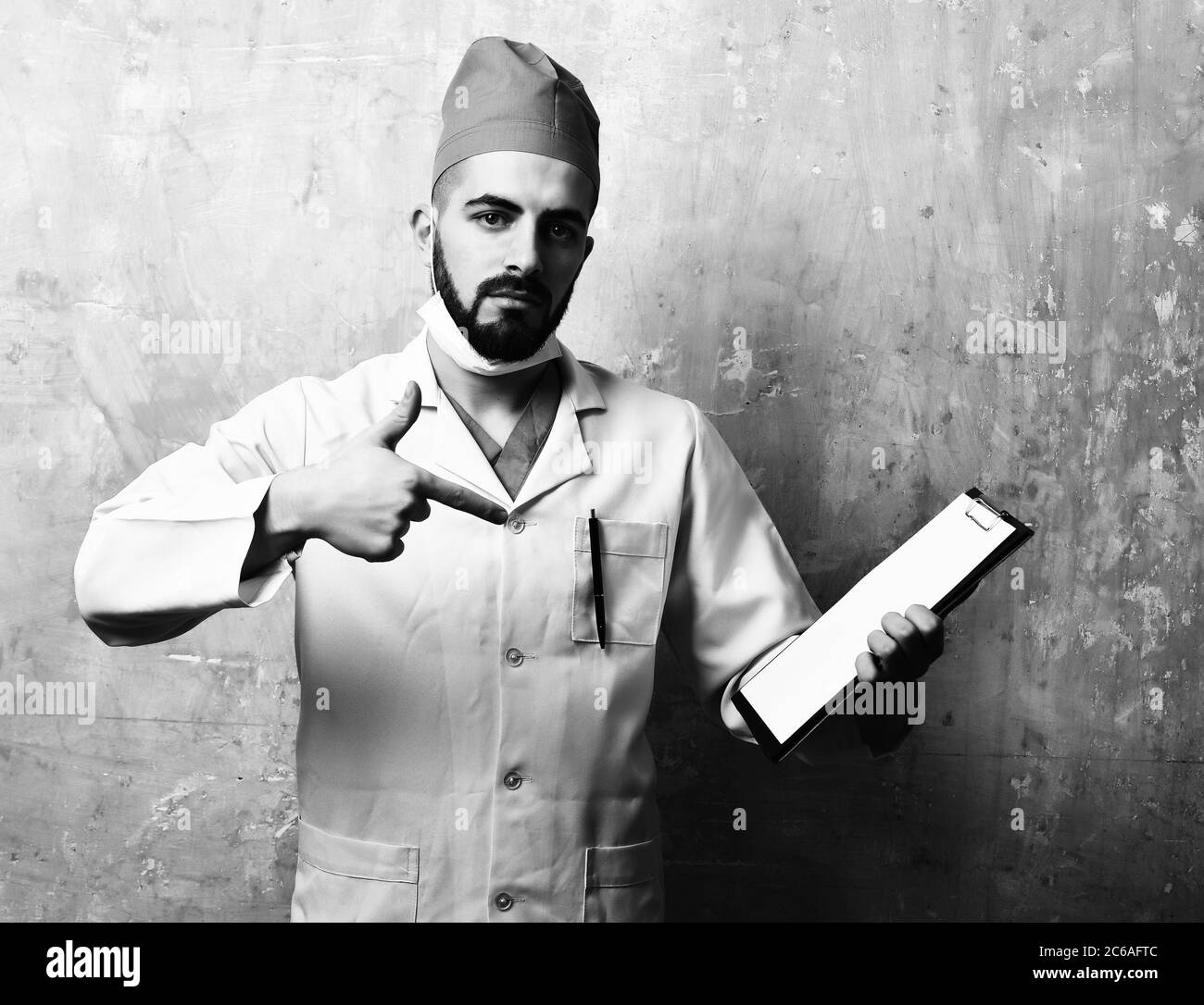 Doctor in uniform with beard and serious face expression pointing at clip folder on background of beige color wall Stock Photo