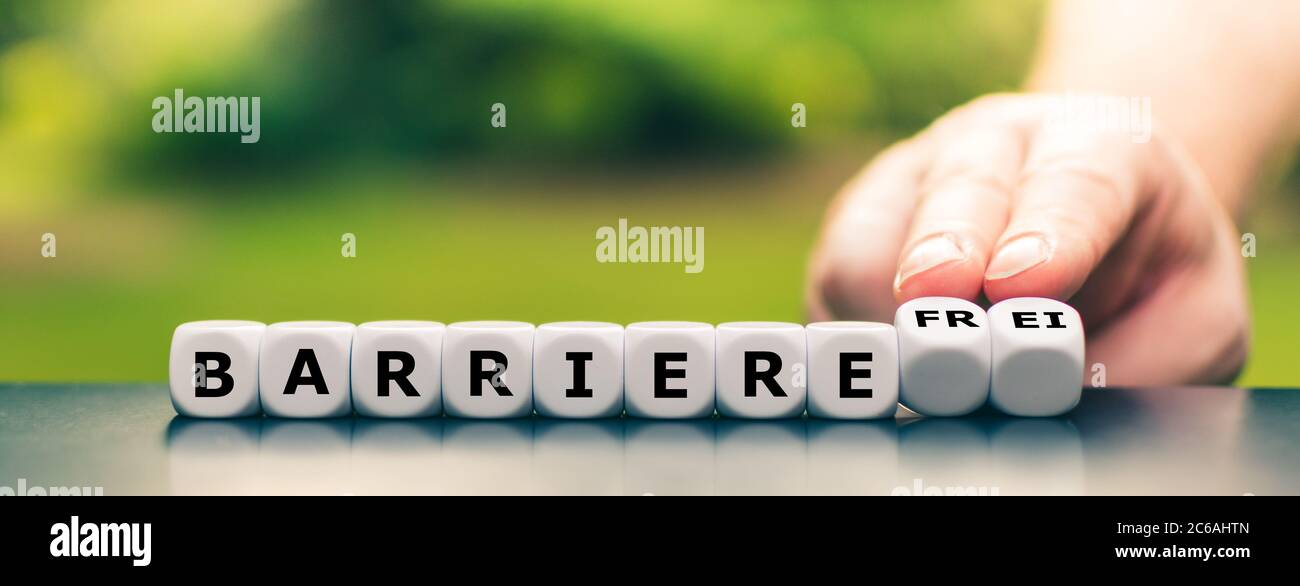 Hand turns dice and changes the German word 'Barriere' (barrier) to 'Barrierefre' (barrier free). Stock Photo