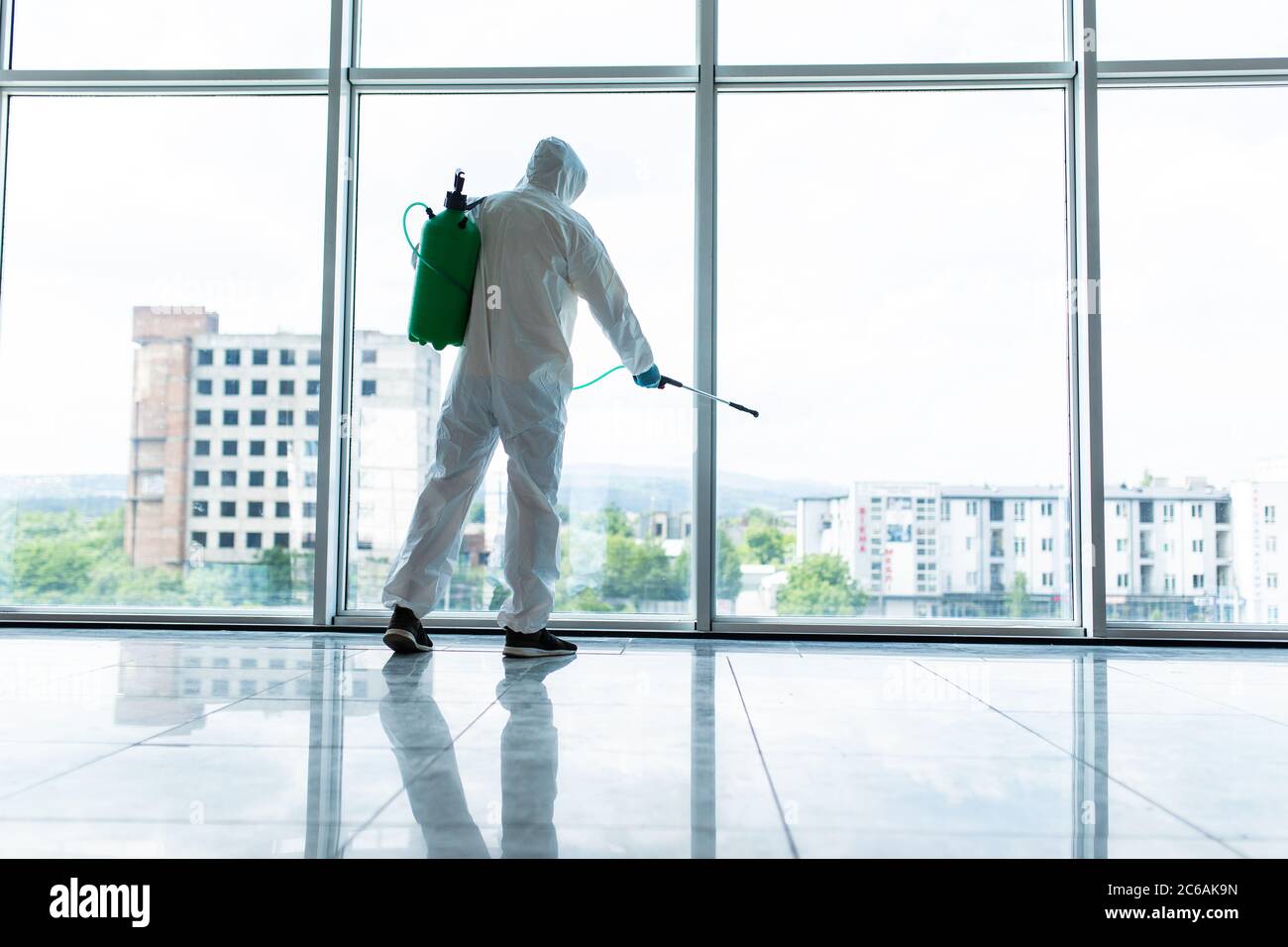 Coronavirus Pandemic. A disinfector in a protective suit and mask sprays disinfectants in office. Protection agsinst COVID-19 disease. Stock Photo