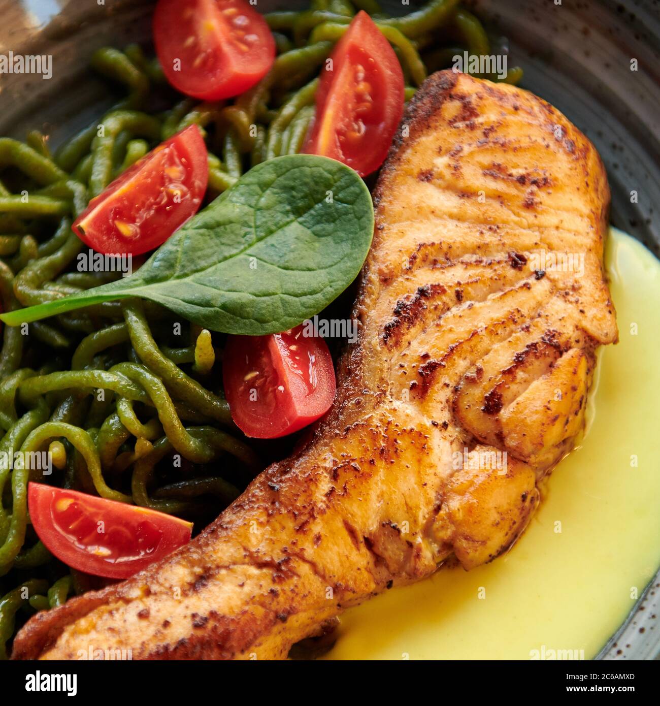 Salmon steak with green pici pasta, cherry tomatoes and cheese sauce. Healthy dish with red fish in the restaurant. Square photo closeup. Stock Photo