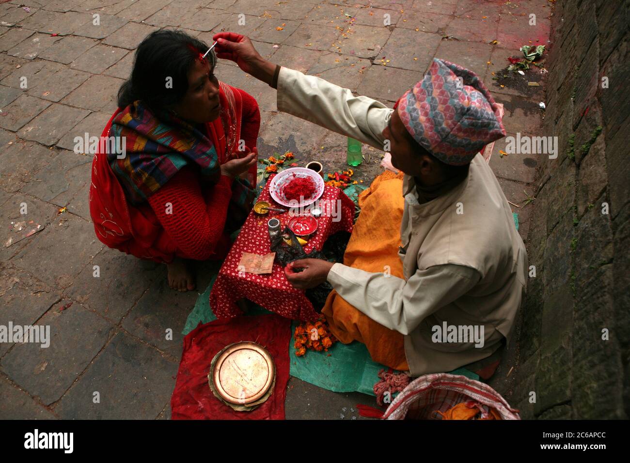 Brahmin applies a tilaka mark on the forehead of a woman next to the entrance to the Dakshinkali Temple near Kathmandu, Nepal. One of the major Hindu temples in Nepal dedicated to the goddess Kali is known for its animal sacrifices which take place in the main sanctuary. Stock Photo