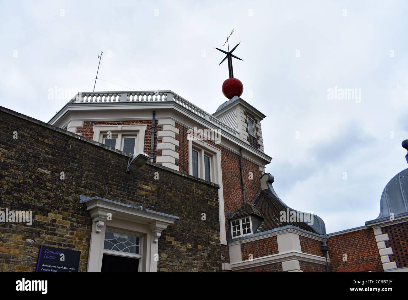 Looking up at the red time ball and weather vane above the Octagon Room and Flamsteed House at the Royal Observatory in Greenwich Park on a cloudy day Stock Photo