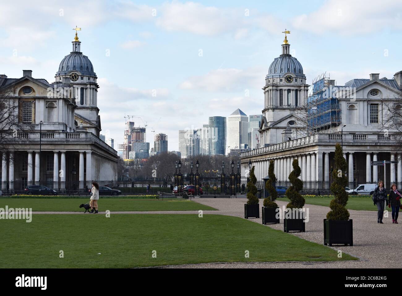 Two of the domed buildings of the Old Royal Naval College looking through to Canary Wharf. A dog walker and two tourists are walking on the grounds. Stock Photo