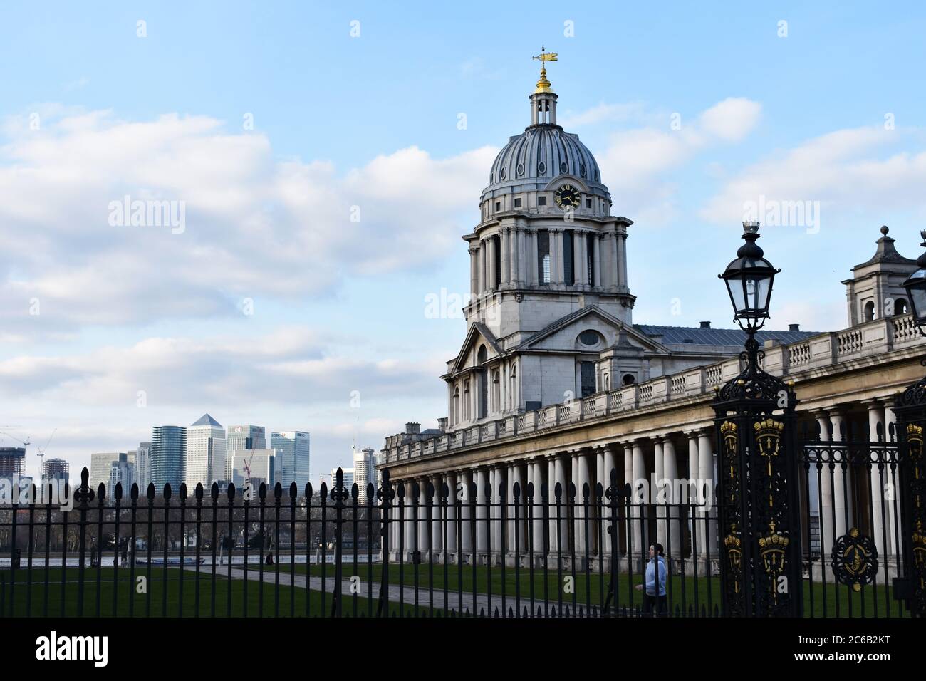 A dome from the Old Royal Naval College is seen.  In the foreground are ornate black railings and old fashioned street lamp.  Canary Wharf is behind. Stock Photo