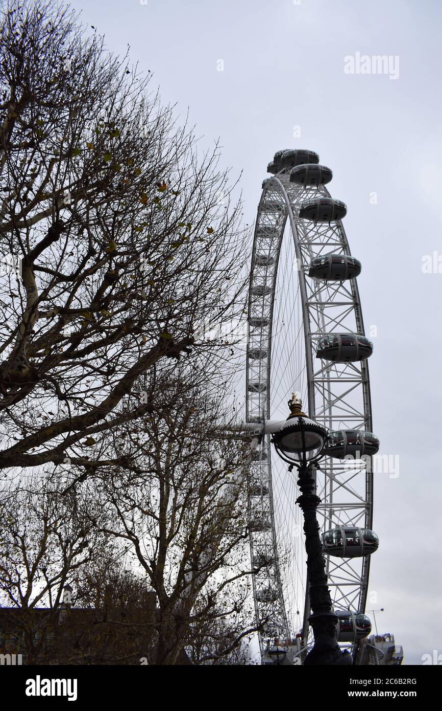 The London Eye.  A giant observation wheel on the South Bank.  Part Of the wheel is shown on a cloudy day, trees and old fashioned street lamp in shot Stock Photo