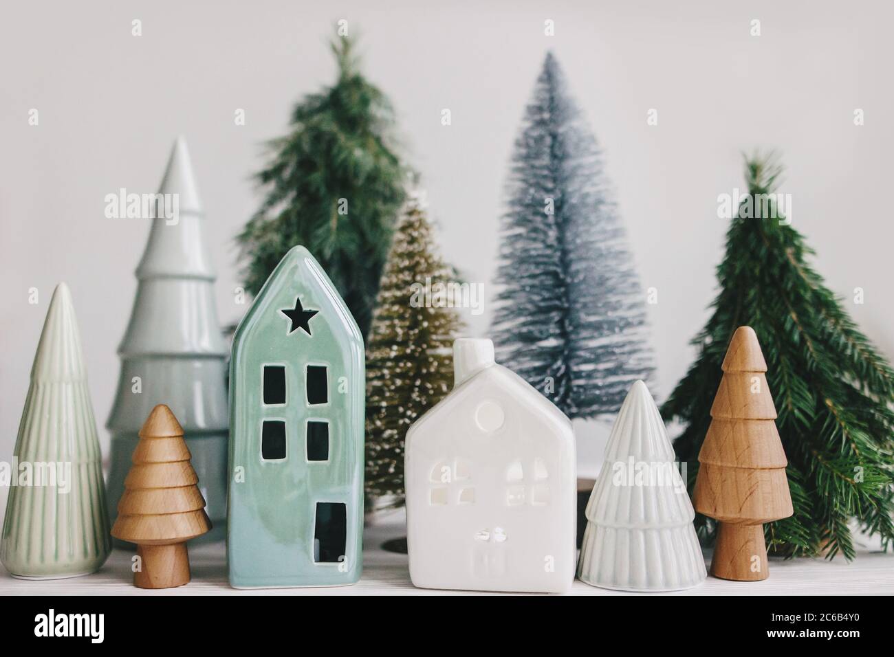 Christmas little houses and trees on white background. Holiday festive decor. Miniature village, ceramic houses, wooden christmas trees and handmade p Stock Photo