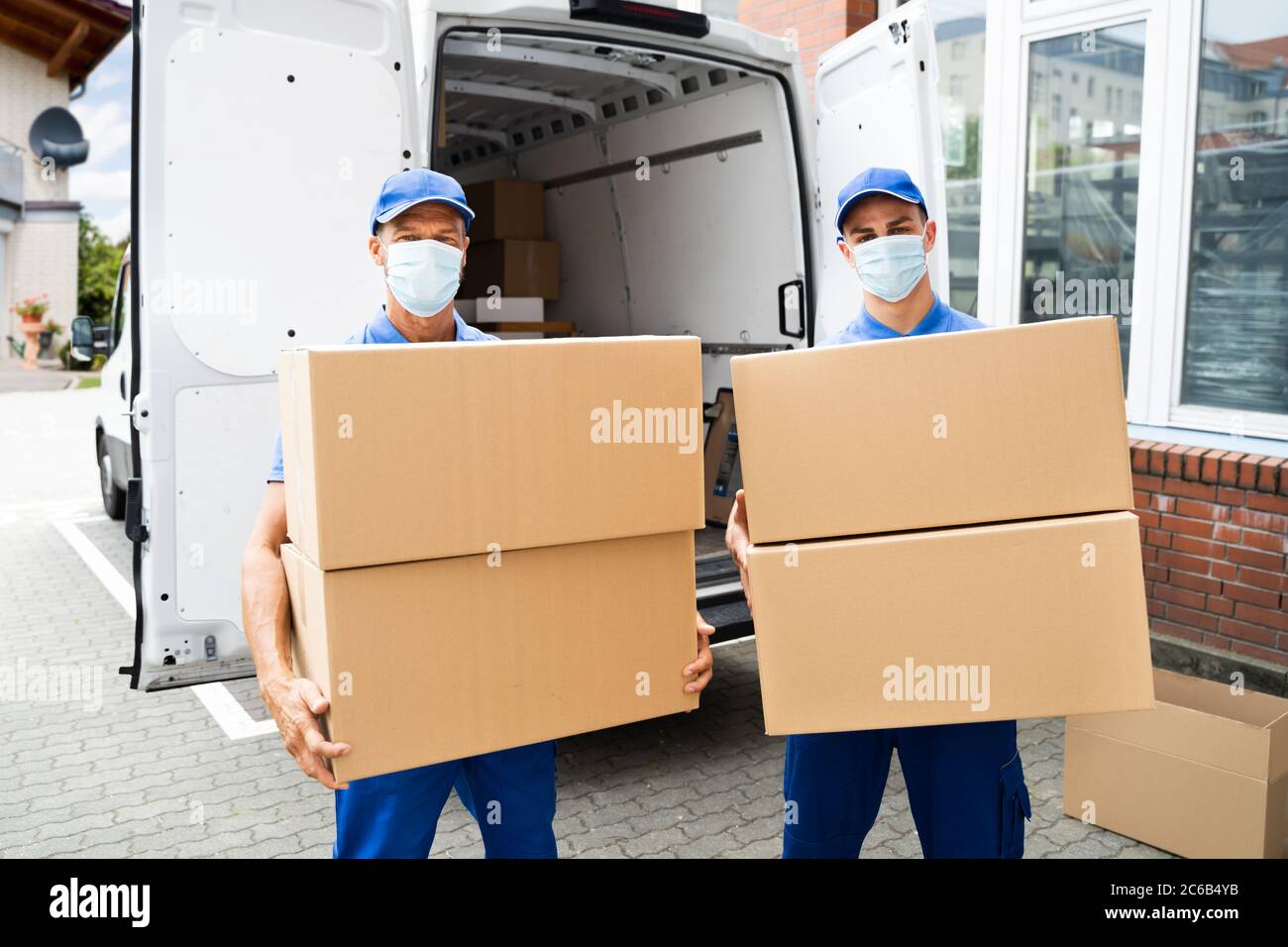 Blue Delivery Men Unloading Package From Truck With Face Mask Stock Photo