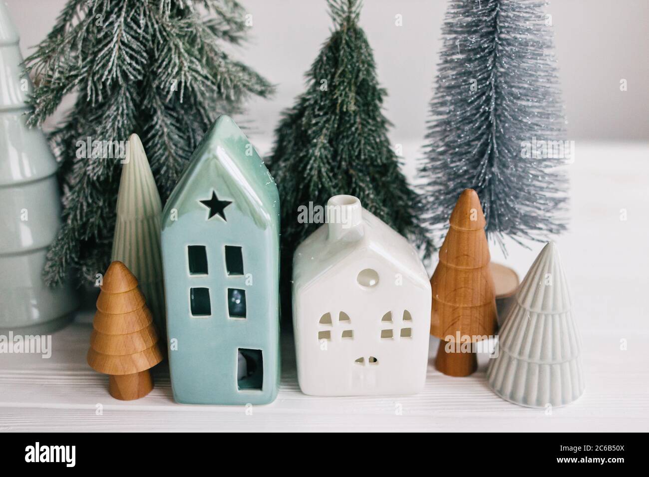 Christmas little houses and trees on white background. Holiday festive decor. Miniature village, ceramic houses, wooden christmas trees and handmade p Stock Photo