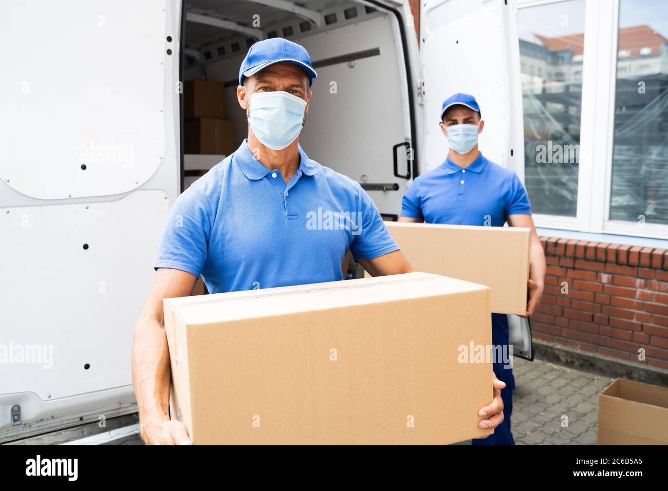 Blue Delivery Men Unloading Package From Truck With Face Mask Stock Photo