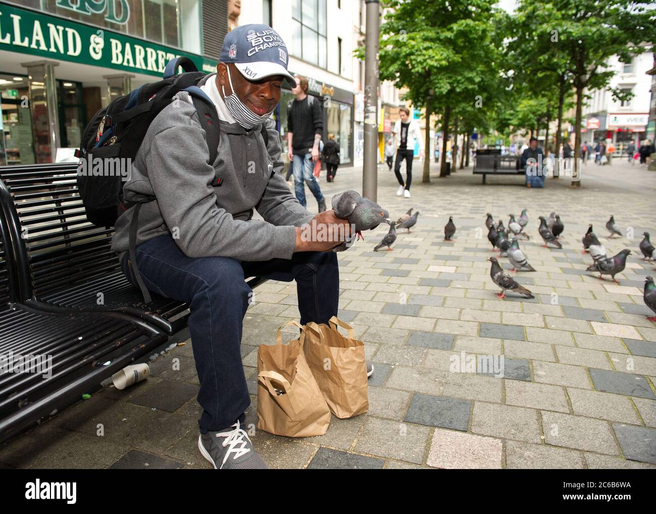 Glasgow, Scotland, UK. 8th July, 2020. Pictured: A man feeds pigeons by hand in Sauchielhall Street of Glasgows shopping district. Credit: Colin Fisher/Alamy Live News Stock Photo