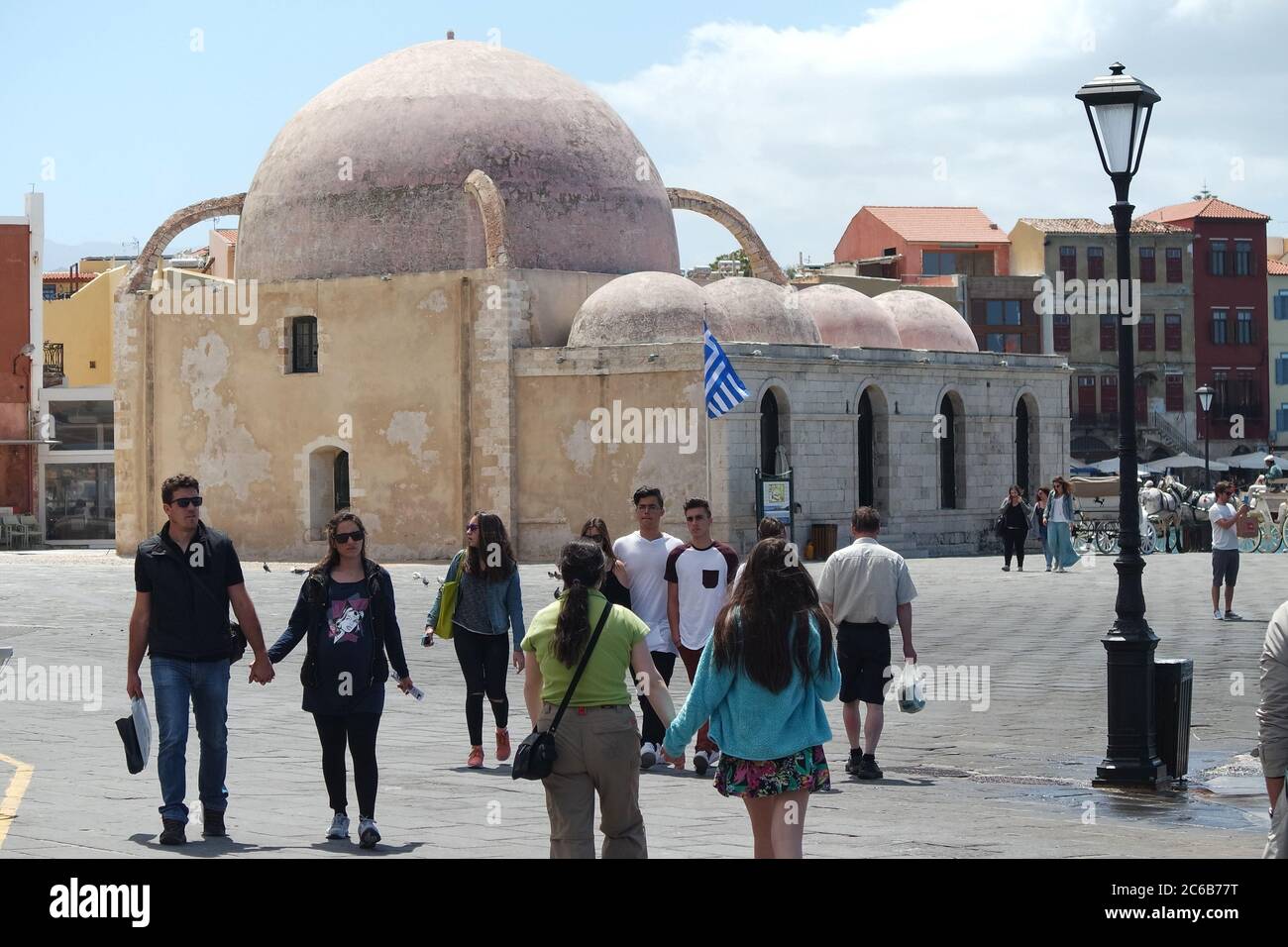 Chania, Crete, Greece. Ancient Mosque at the Venetian harbor. Holiday makers wander by.  Landscape aspect.  Copy space. Stock Photo