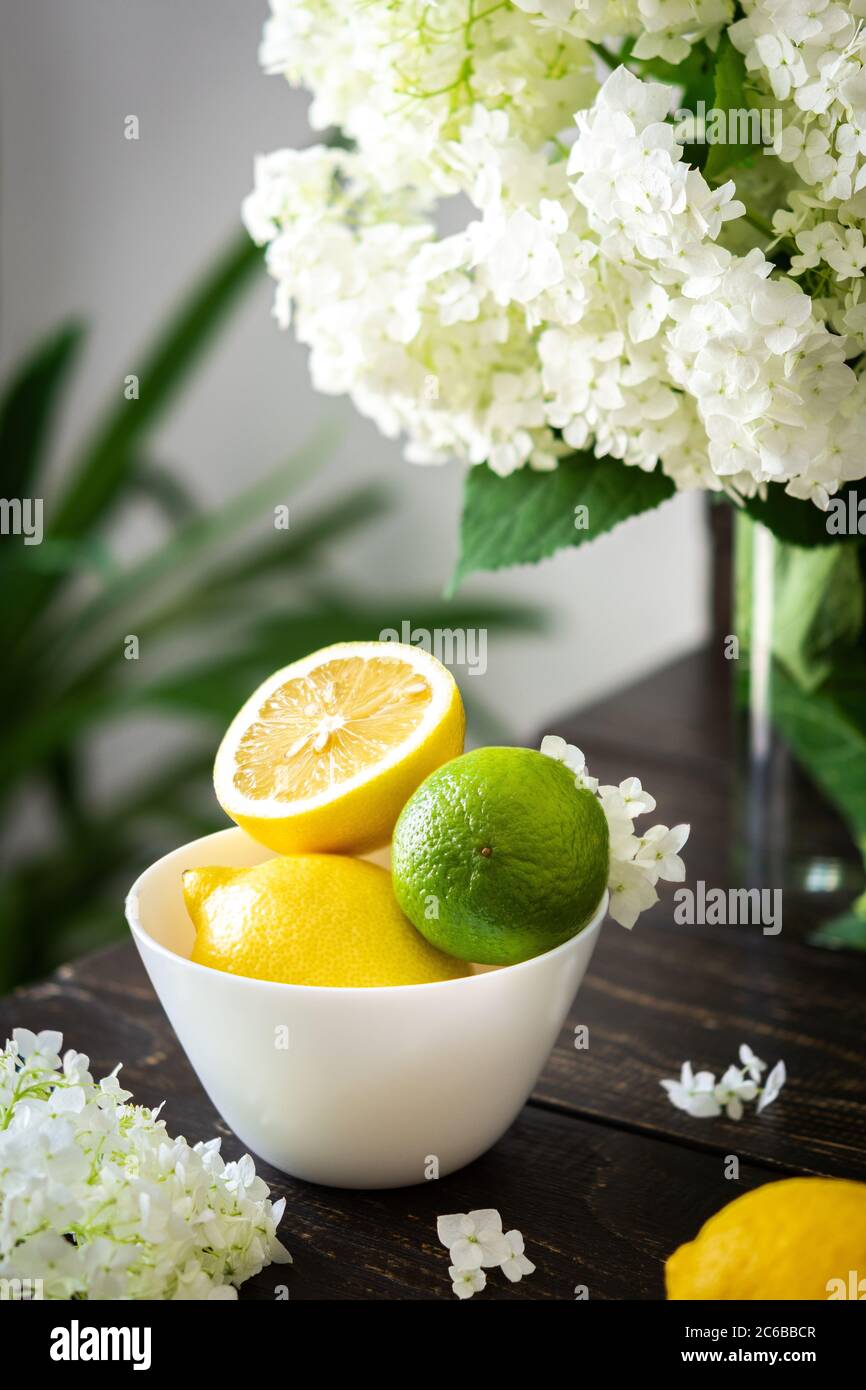 Vase of flowers viburnum opulus Roseum and plate with lemons and lime Stock Photo