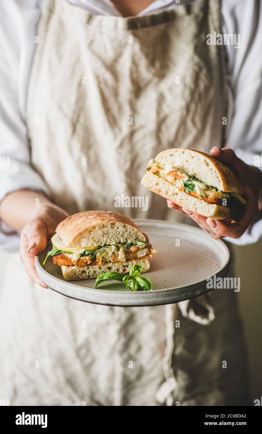 Woman holding fresh breakfast sandwich with fried fish, lemon, arugula Stock Photo