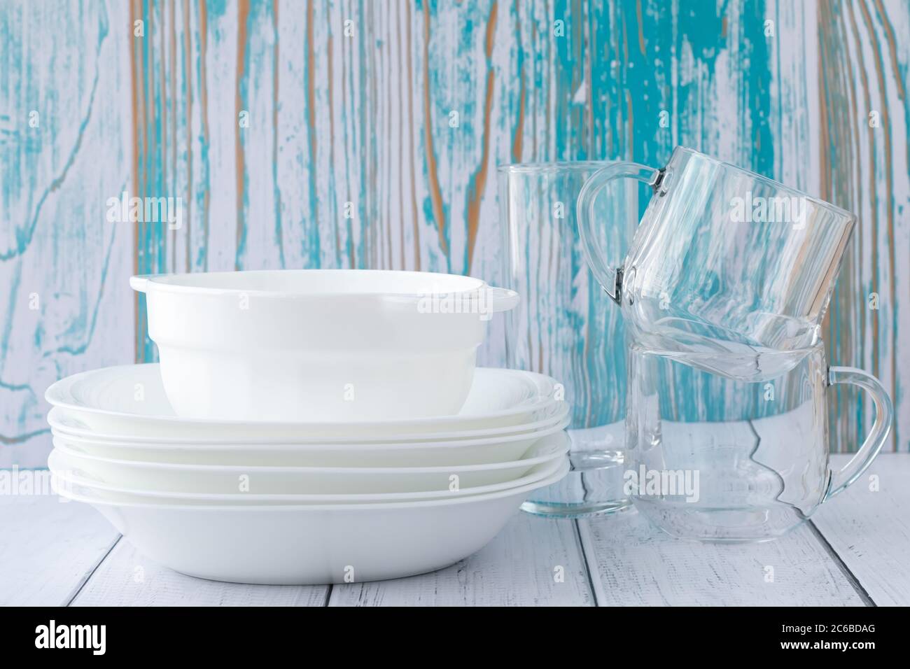 White bowls, glasses and plates on the table. Stack of clean dishes on a blue wooden background Stock Photo