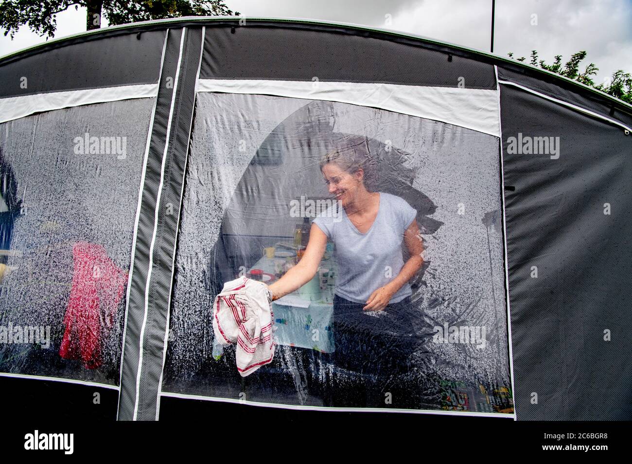 A woman camper is seen cleaning the morning mist off her tent during the summer holidays.Due to the coronavirus crisis, many Dutch citizens have taken to touring their own country during the summer holidays, many of them are seen at camping Ons Buiten in Oostkapelle, Zeeland. Stock Photo