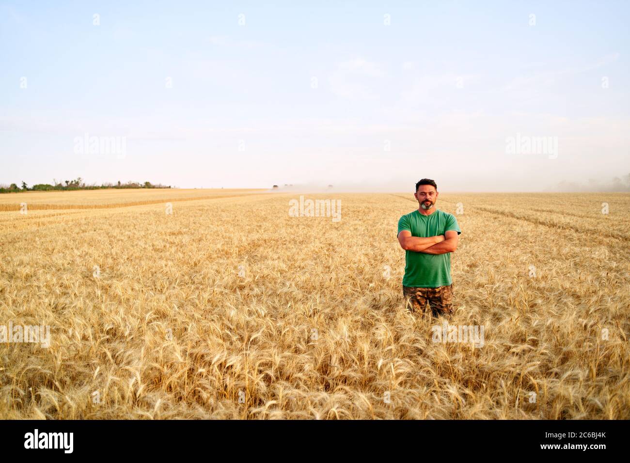 Happy farmer proudly standing in wheat field with arms crossed on chest ...