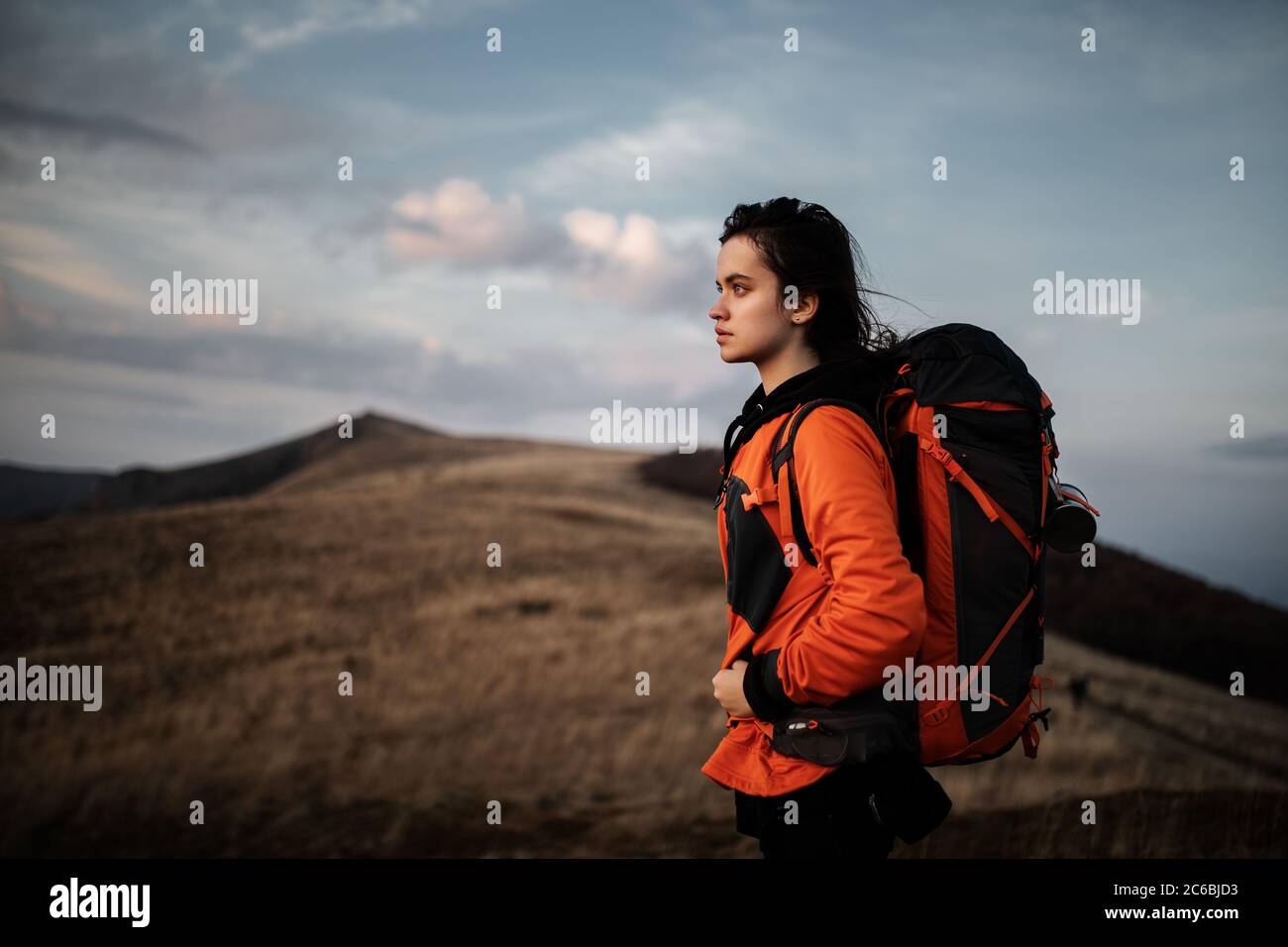 young woman hiker with a backpack travels the mountains and admires the ...