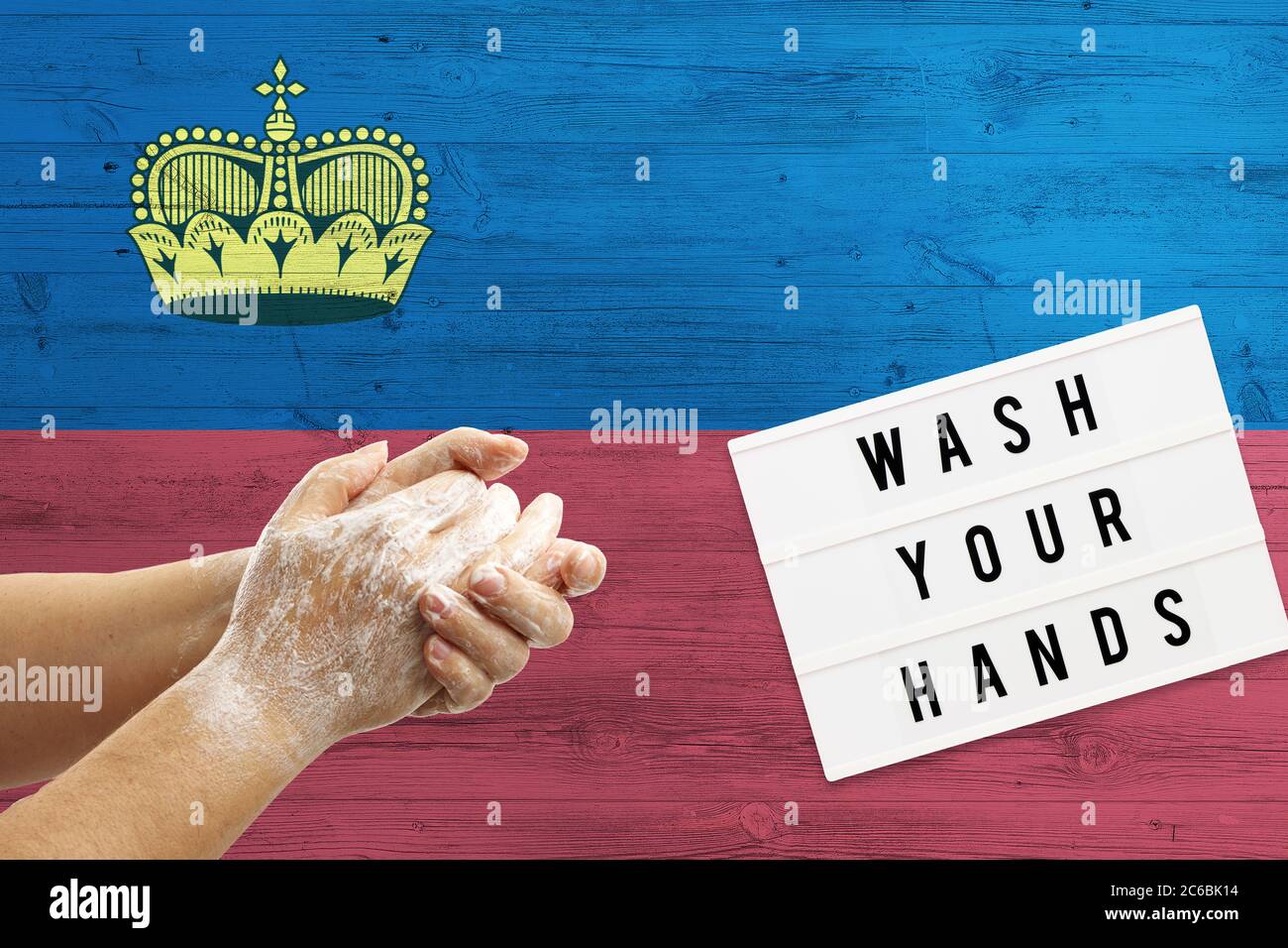 Liechtenstein flag background on wooden surface. Minimal wash your hands board with minimal international hygiene concept hand detail. Stock Photo