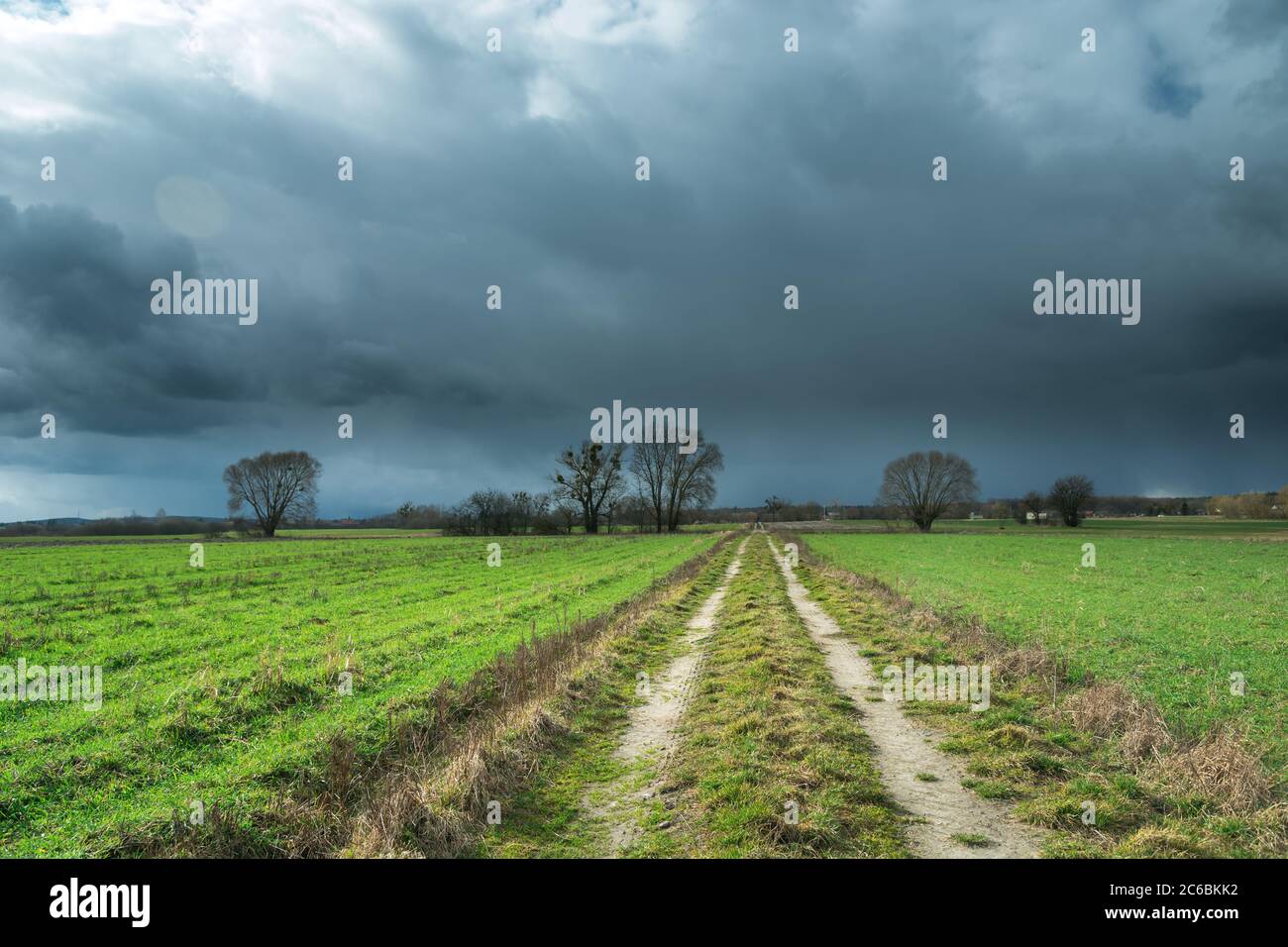 Spring storm dark clouds and a dirt road through green fields Stock ...