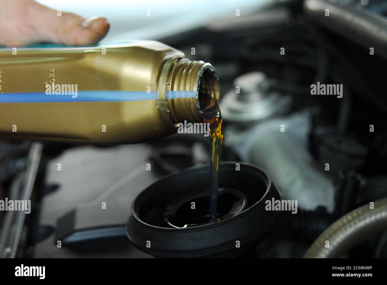 Adding Oil to a Car, man's hand holding a bowl of motor oil and poured