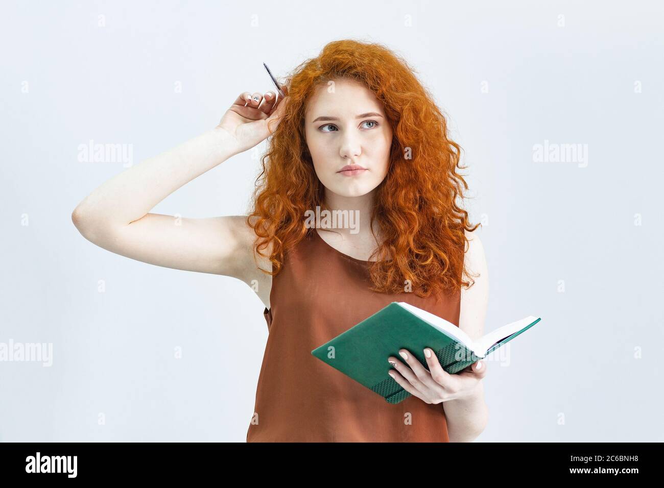 Let me think. A Studio shot of a pretty red-haired girl looking sideways with a thoughtful and sly expression on her face, as if she had a good idea p Stock Photo