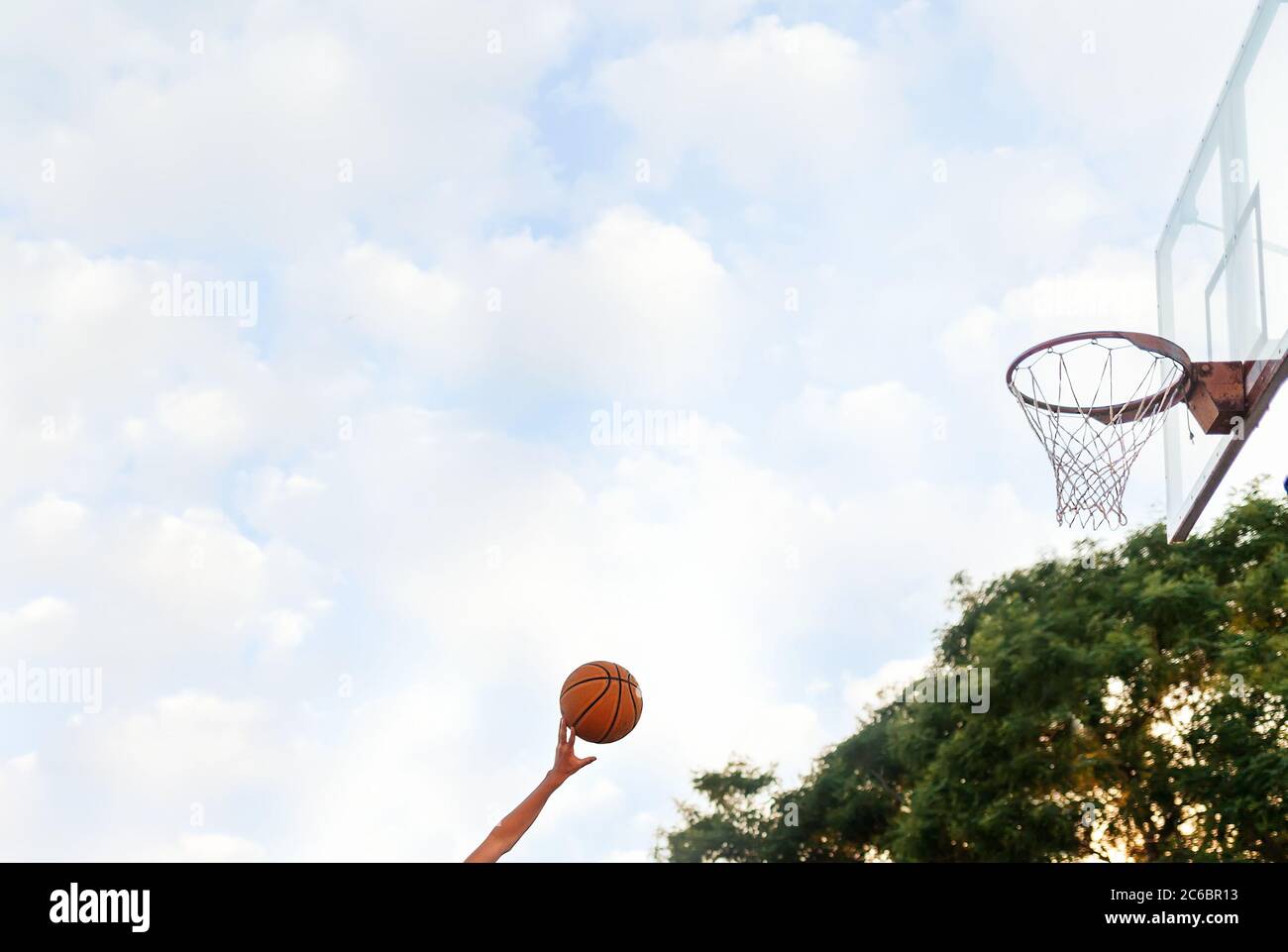 The hand throws the ball into the basketball Hoop. Side view. Sky with