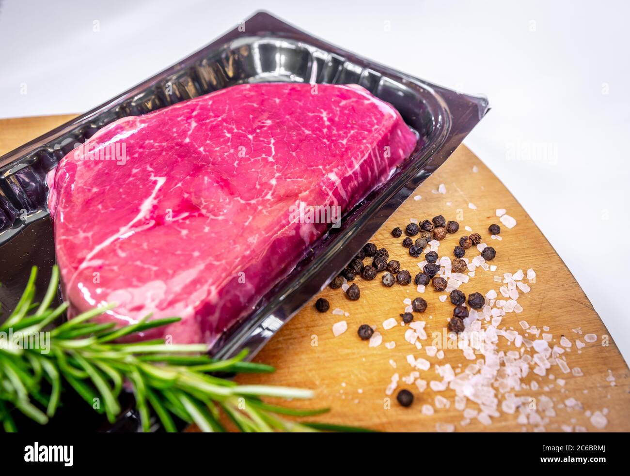 Vacuum-packed beef steak and spices on wooden chopping board Stock Photo